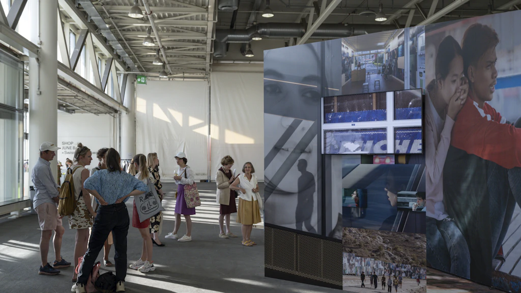 Des visiteurs se tiennent dans une halle d’exposition à côté d’une installation grand format composée de photographies et d’écrans.
