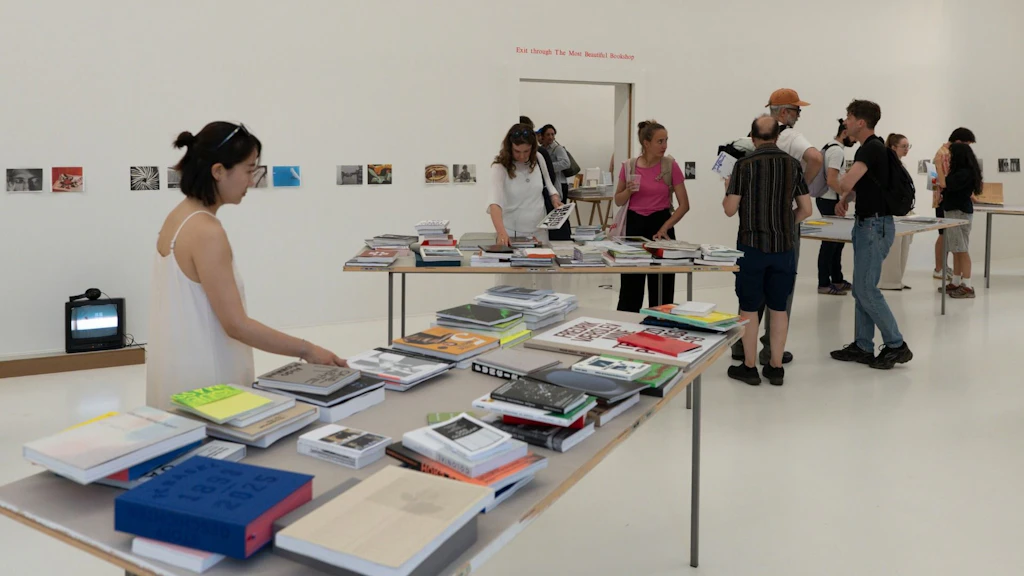 Luminoso spazio espositivo con più visitatori che osservano i libri della mostra «I più bei libri svizzeri». Numerose pubblicazioni sono esposte sui tavoli, mentre gli ospiti si muovono nello spazio e si scambiano idee.