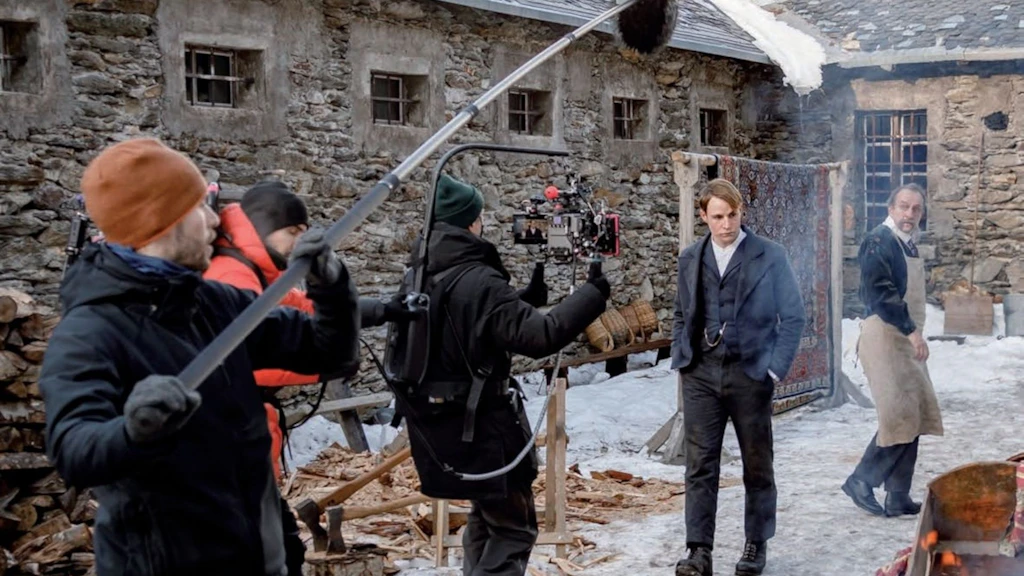 Tournage de la série « Winter Palace ». Une équipe de tournage avec caméra et perche sonore filme des acteurs en costumes historiques dans une cour enneigée entourée de bâtiments en pierre.