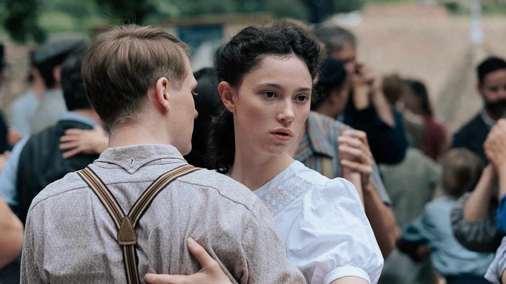 Scène du film « À bras le corps » : un jeune couple danse étroitement enlacé en plein air, entouré d’autres danseurs et danseuses. La femme regarde sur le côté.