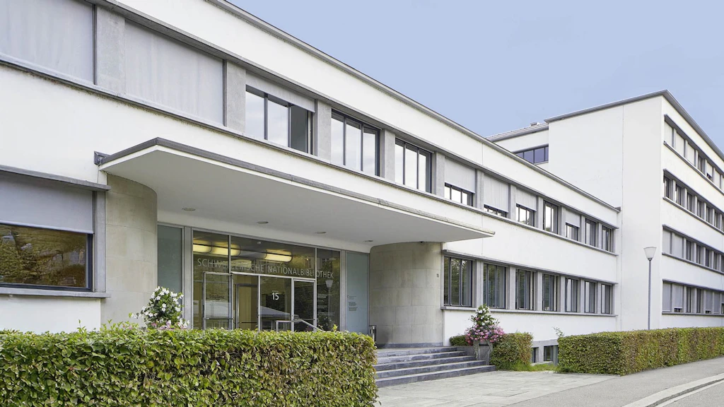 Aussenansicht der Schweizerischen Nationalbibliothek, modernes weisses Gebäude mit Eingangsbereich, Fenstern und Hecke.