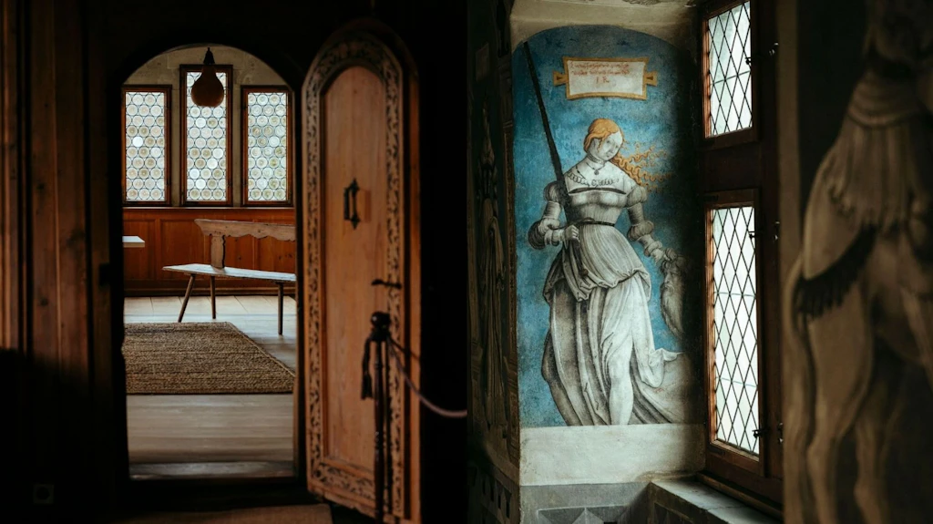 Blick durch eine offene Holztür in historische Räume des Museums Kloster Sankt Georgen in Stein am Rhein, mit Täfer, bleiverglasten Fenstern und Wandgemälde.