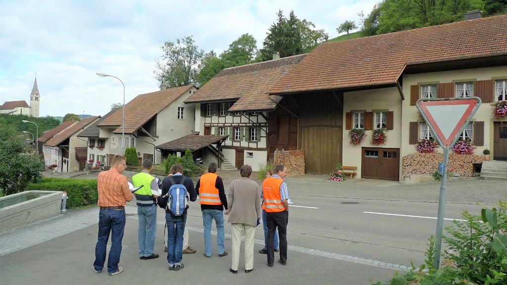 Das Bild zeigt eine Gruppe von Inventarisatorinnen und Inventarisatoren bei der Begutachtung einer Häuserzeile in einem Dorf im Kanton Aargau.