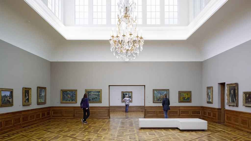 Blick in den grossen Ausstellungssaal der Sammlung Oskar Reinhart «Am Römerholz» mit Parkettboden, Kronleuchter und Gemälden an den Wänden. Einzelne Besucherinnen und Besucher betrachten die ausgestellten Werke.