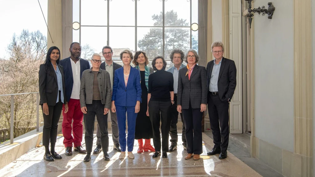 Zehn Personen stehen gruppiert auf einer Terrasse vor einem großen Fenster, die Mitglieder der Kommission für historisch belastetes Kulturerbe.
