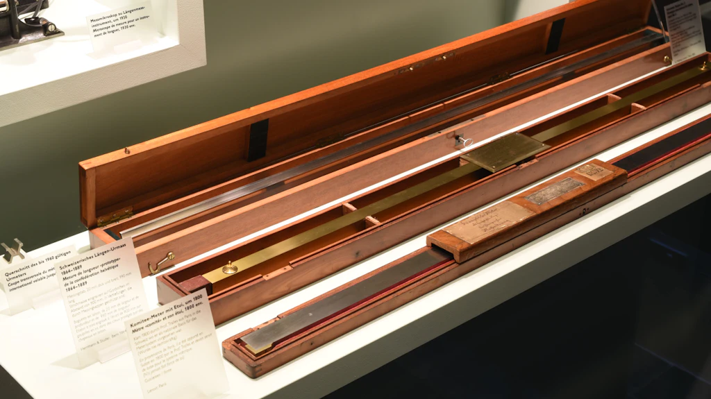 L’image montre des longues boîtes en bois dans lesquelles sont conservés trois mètres en métal : la copie No 2 du mètre étalon de Paris qui a été la norme jusqu’en 1960, la « mesure de longueur » de la Confédération au 19e siècle et le mètre « comité » datant de 1800 environ.