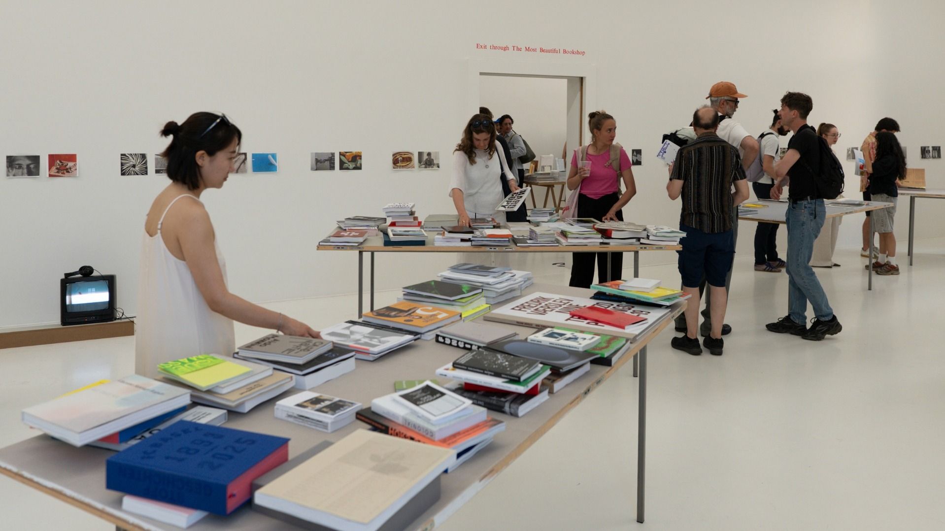 Espace d’exposition lumineux avec plusieurs visiteurs consultant les livres de l’exposition « Les Plus Beaux Livres Suisses ». De nombreuses publications sont disposées sur des tables, tandis que les visiteurs se déplacent et échangent dans l’espace.