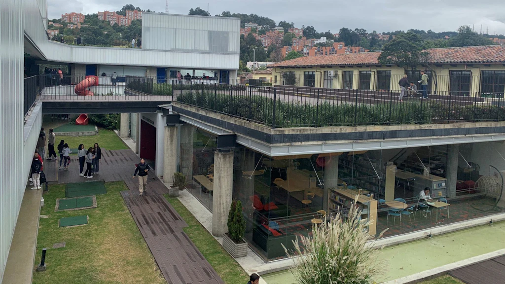 Campus de l’École suisse de Bogotá avec des bâtiments modernes vitrés, des terrasses végétalisées et une cour intérieure ; des élèves circulent entre les bâtiments, avec en arrière-plan le paysage urbain vallonné.
