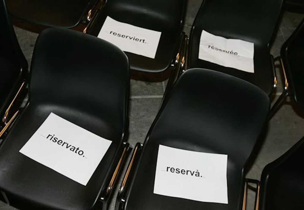 Plusieurs chaises noires avec des panneaux de réservation blancs dans les quatre langues nationales suisses : « reserviert », « réservée », « riservato » et « reservà ».