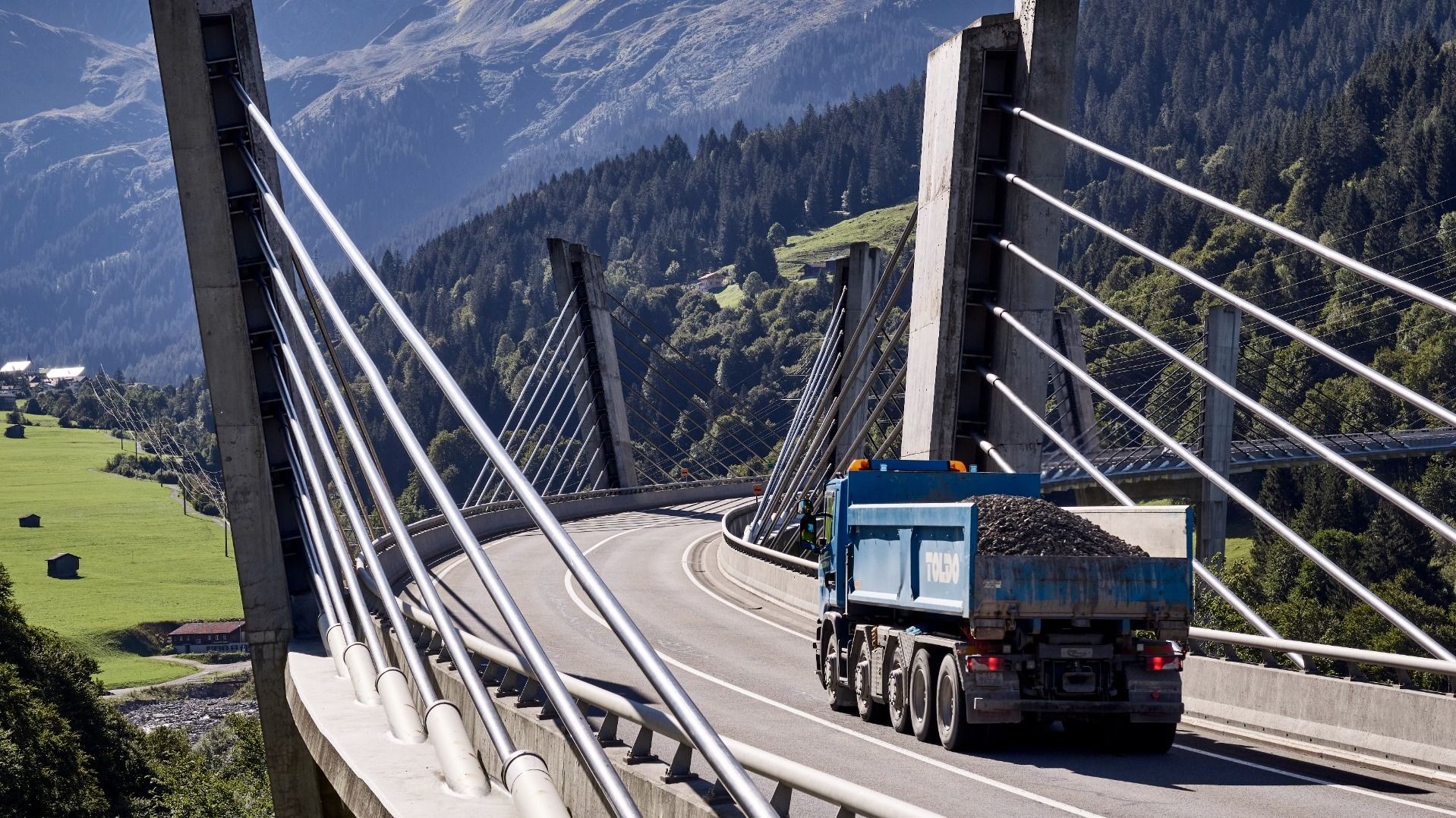 Un camion si dirige sul ponte Sunniberg verso un paesaggio di montagna. L’immmagine trasmette un’atmosfera di partenza.