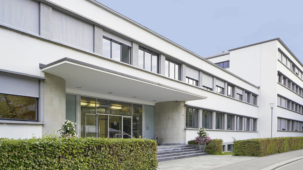 Vista esterna della Biblioteca nazionale svizzera, moderno edificio bianco con ingresso, finestre e siepe.