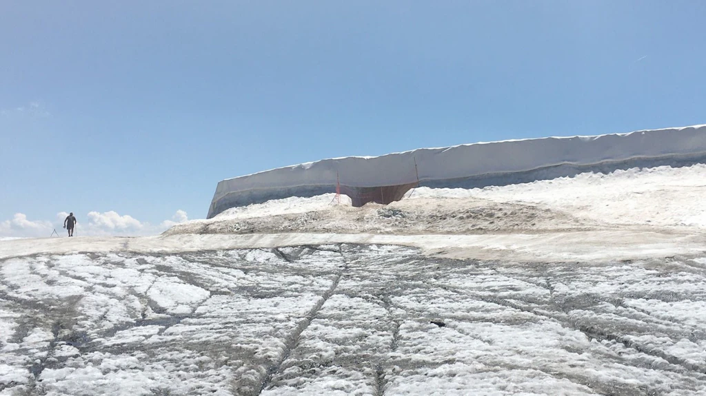 Questa immagine mostra un ghiacciaio coperto da un sottilissimo involucro di ghiaccio su cui è conservata una riserva di neve molto grande e lunga, avvolta in un telo bianco.