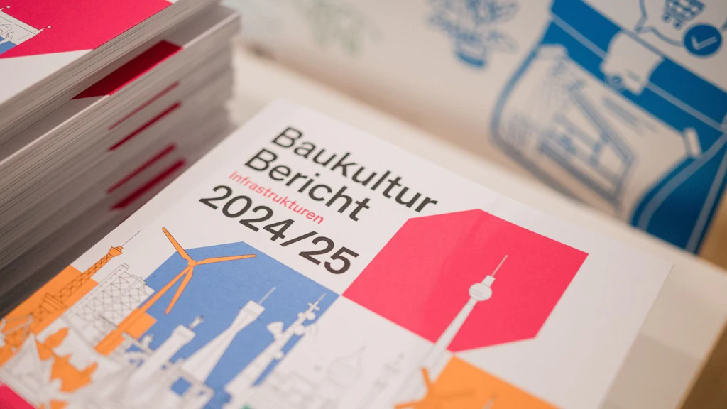 Ein Stapel des Baukultur Berichts 2024/25 mit grafischen Illustrationen von Infrastrukturen auf dem Cover. Das Buch liegt auf einem Tisch, im Hintergrund sind weitere Broschüren sichtbar.